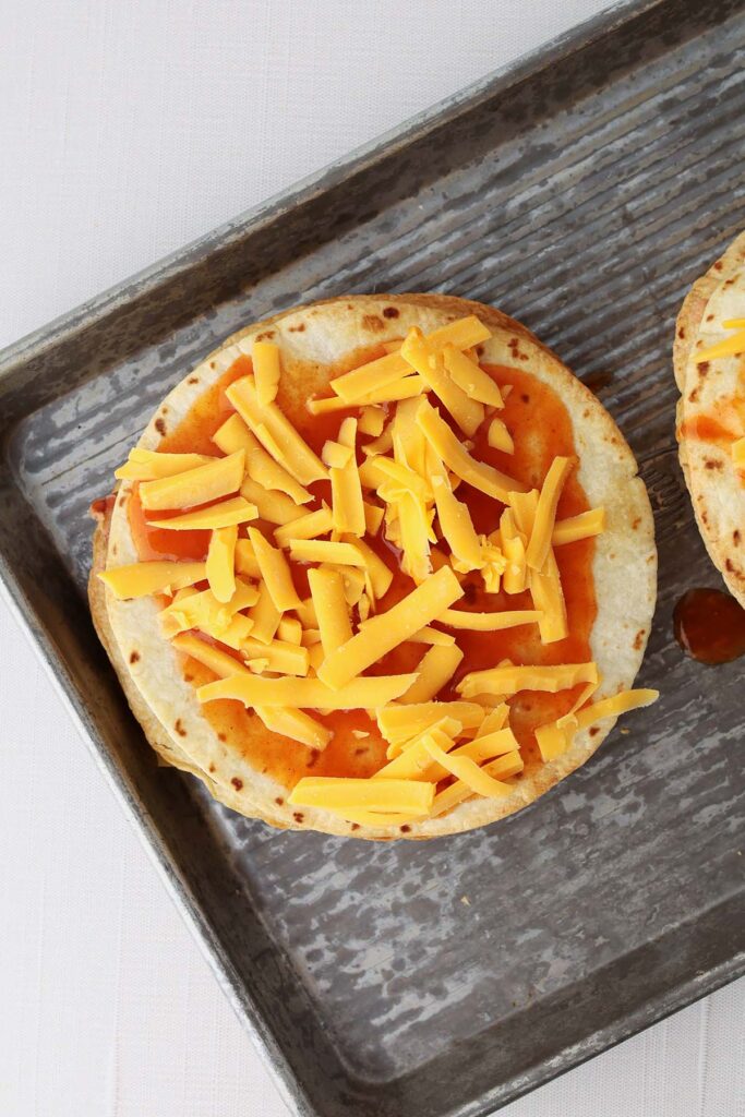 Top down image showing a crispy baked tortilla spread with enchilada sauce and cheese