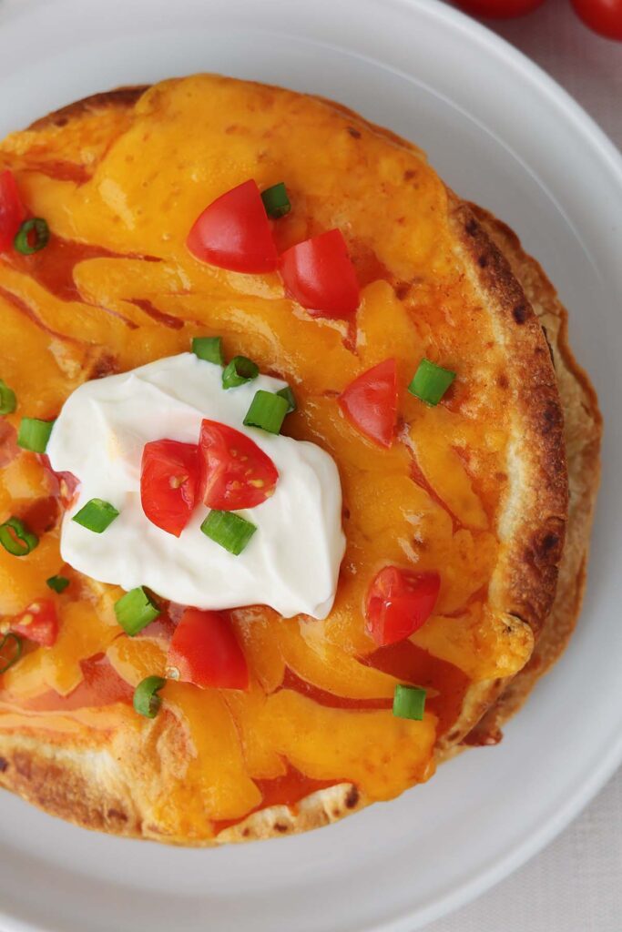 Close up top down image showing a tortilla that is crispy with sauce, cheese, tomato and green onion on a white plate
