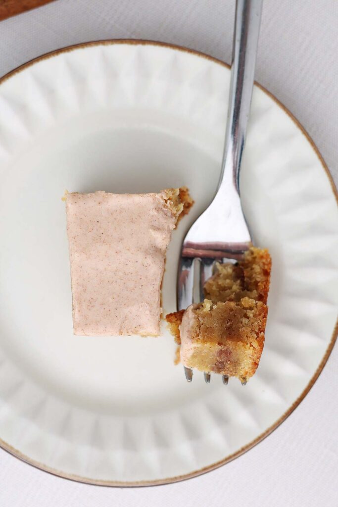 Top down image showing a white plate with a brown edge that is holding a bar with a cinnamon glaze and bite on a fork