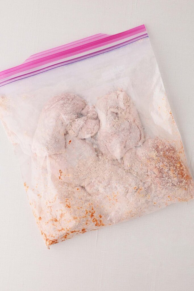 Top down image showing a plastic zip top bag with chicken that is coated in flour and seasonings