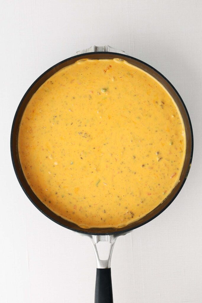 Creamy Velveeta queso with sausage and peppers melted in a skillet, shown from above on a white background.