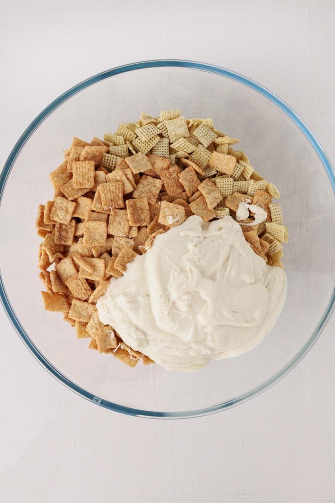 Top down image showing a glass bowl filled with chex, cinnamon toast crunch, and melted white chocolate