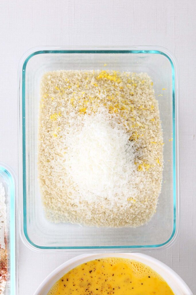 Top down image showing a glass rectangle dish with breadcrumbs, parmesan cheese, and lemon zest