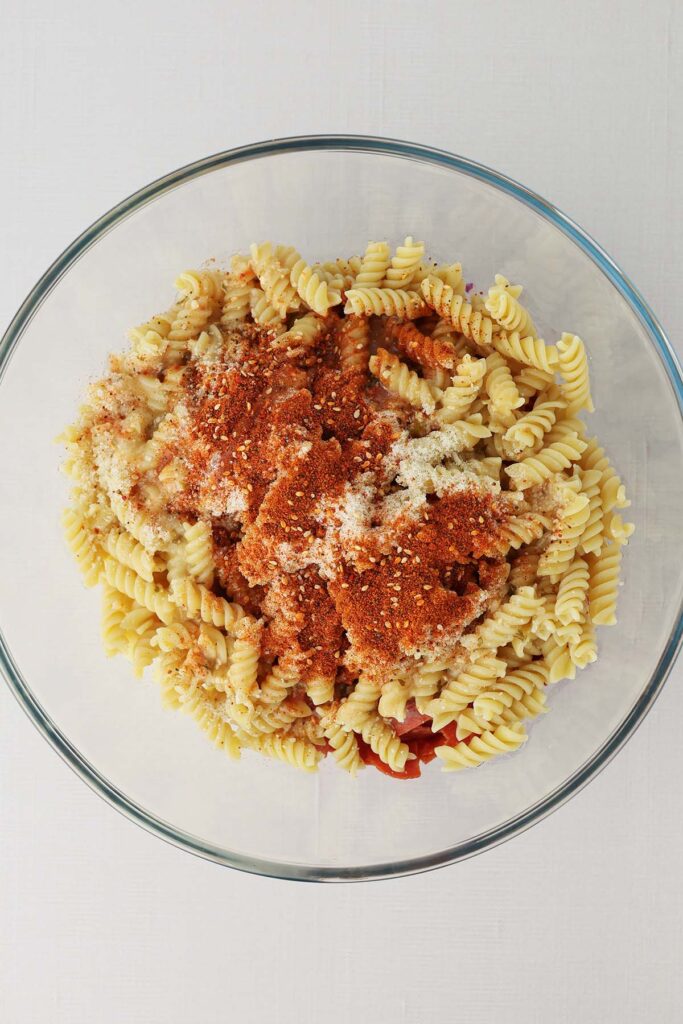 Top down image showing a glass bowl filled with spiral pasta that is sprinkled with seasoning and cheese