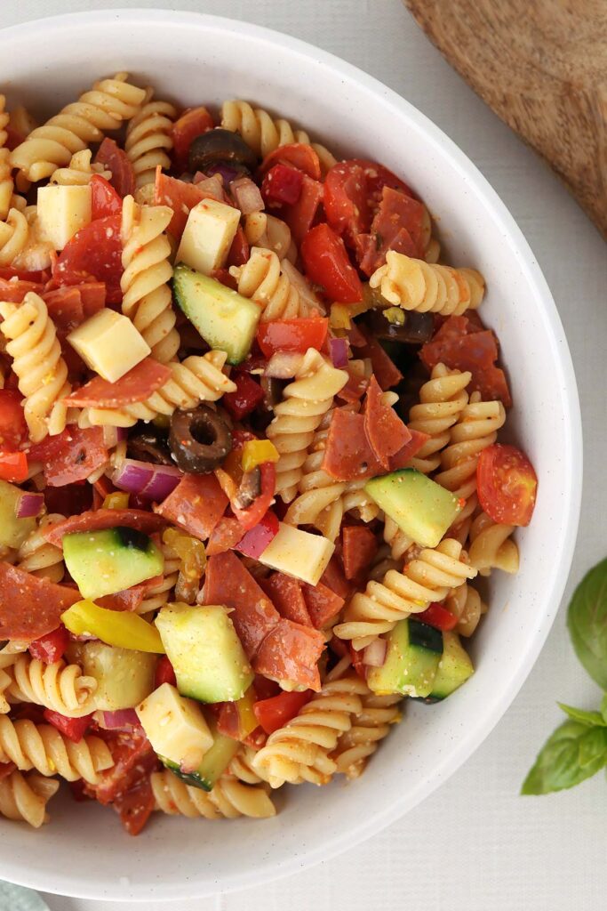 Top down image showing a white bowl filled with spiral pasta, vegetables, and pepperoni
