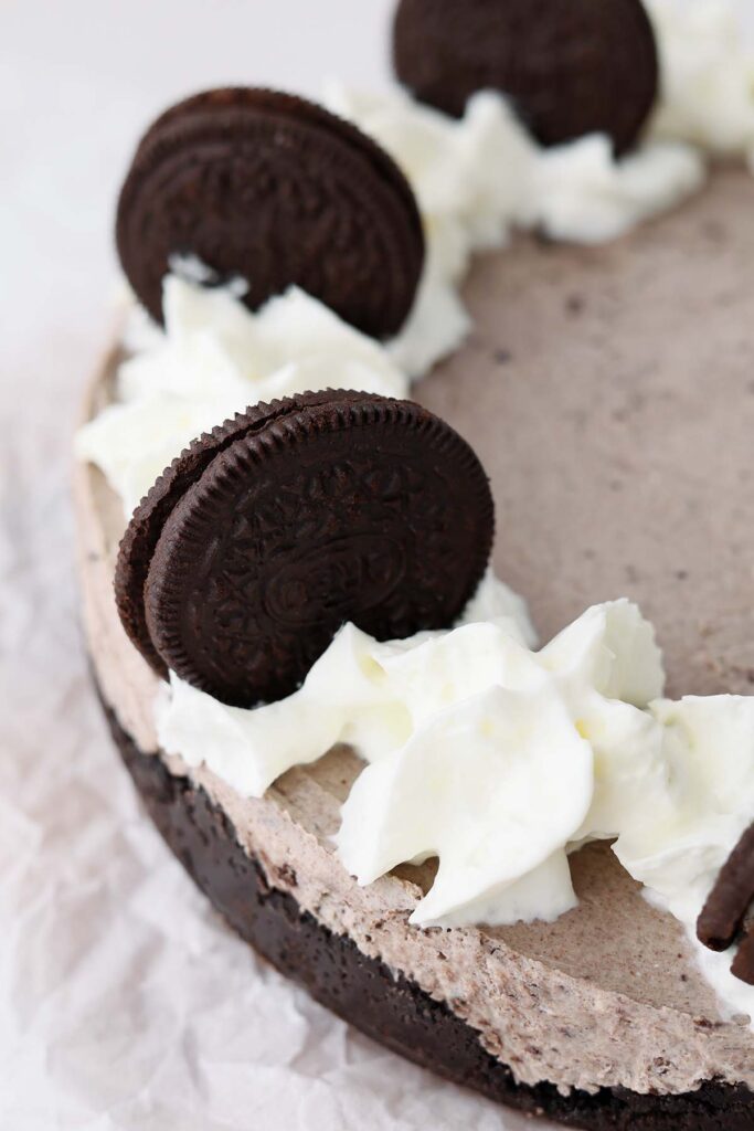 close up image showing a cookies and cream no bake cheesecake with whipped cream and oreo cookies on tip