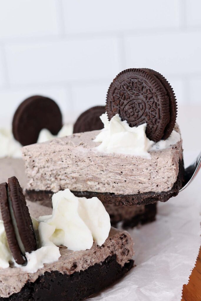 close up image showing a slice of cheesecake being pulled from an entire cake with a fork. Whipped cream and oreo on top.