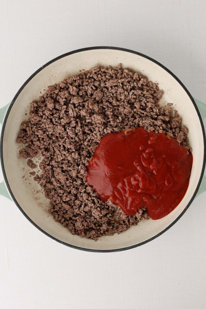 Top down image showing cooked ground beef in a pan with a red sauce