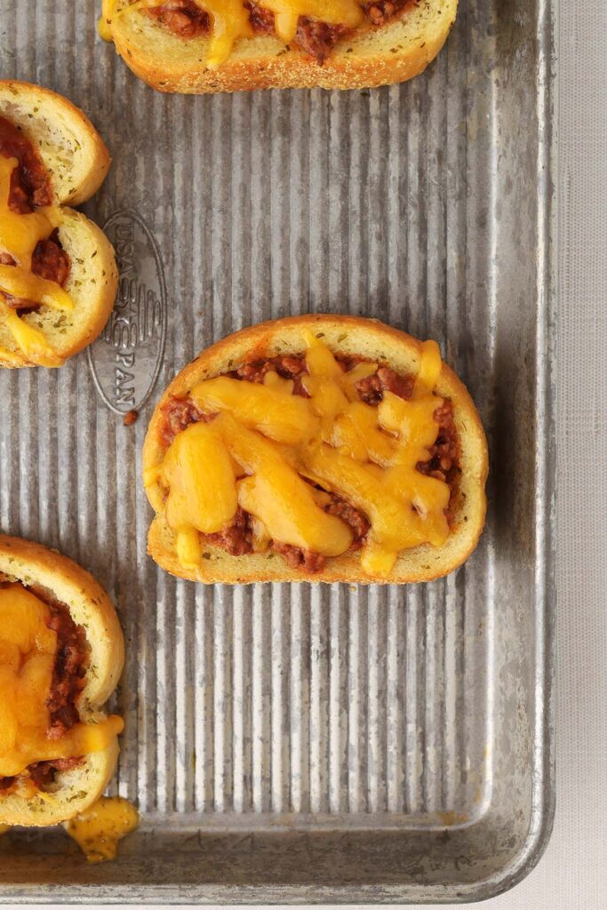 close up image showing a baking tray filled with garlic bread that is topped with a beef mixture and melted cheese
