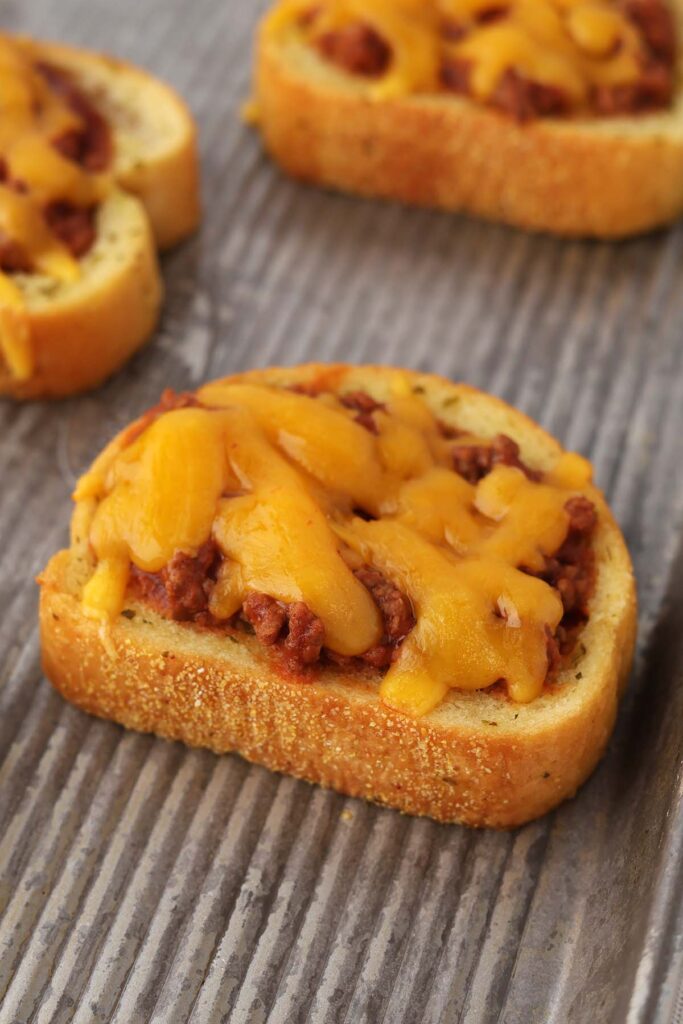 close up image showing a baking tray filled with garlic bread that is topped with a beef mixture and melted cheese