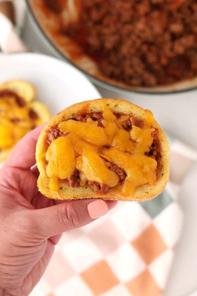 Top down image showing a hand holding a garlic toast that is topped with a beef mixture and melted cheese