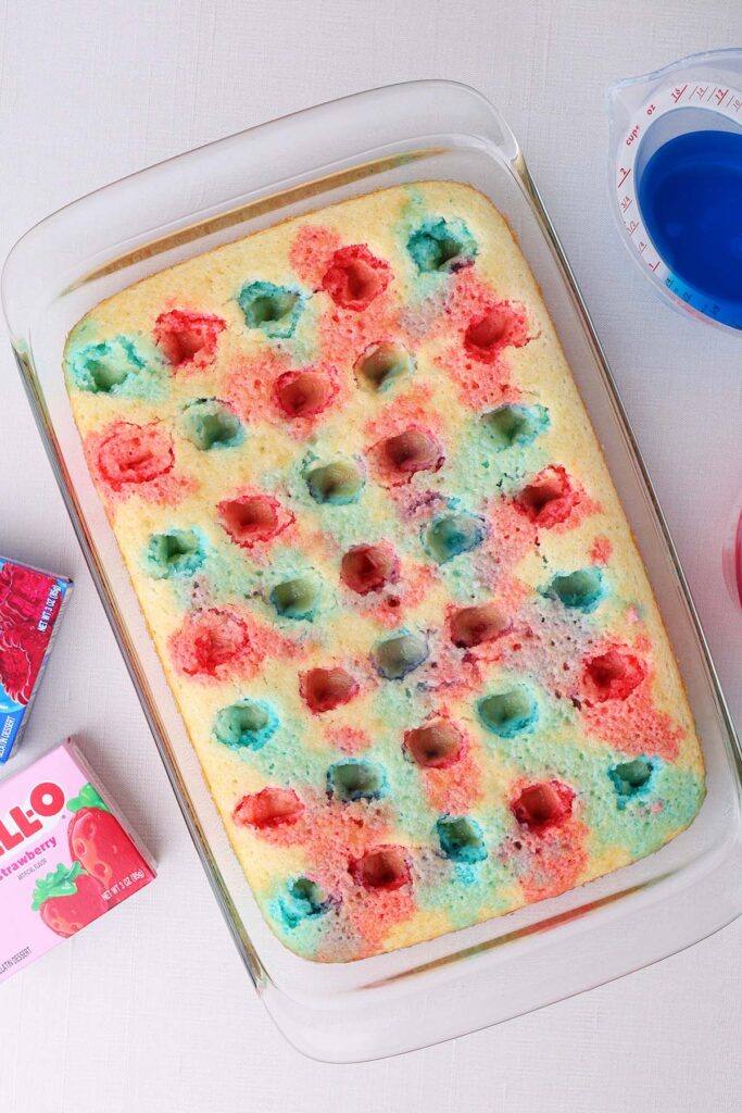 top down image showing a glass pan with a cake that has holes poked in it and red and blue liquid alternating each hole
