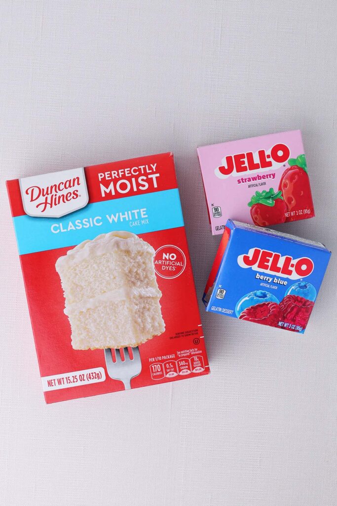 Top down image showing a box of duncan hines classic white cake mix, jello strawberry, jello berry blue