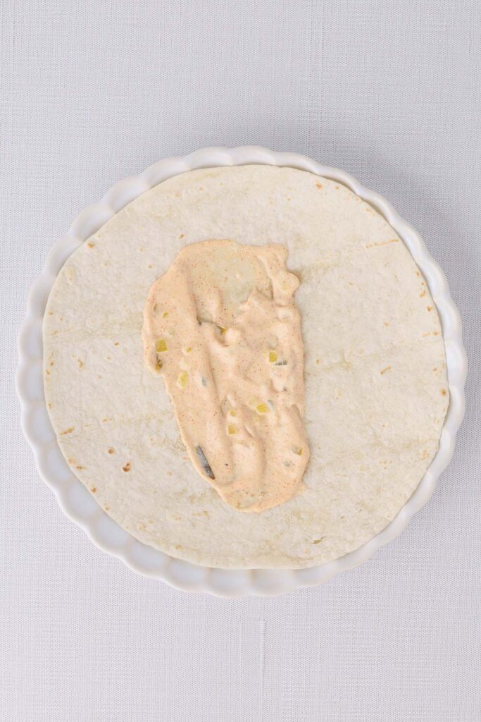Top down image showing a tortilla on a white plate with burger sauce spread