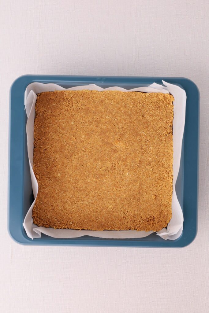 Overhead view of a baked graham cracker crust in a parchment-lined square baking pan.