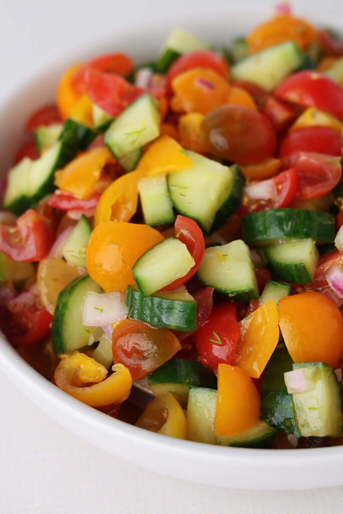 close up image showing chopped cucumber, tomato and onion in a white bowl