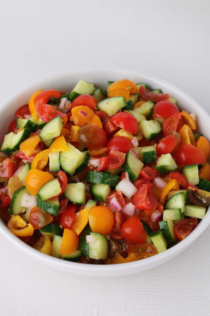 close up image showing chopped cucumber, tomato and onion in a white bowl