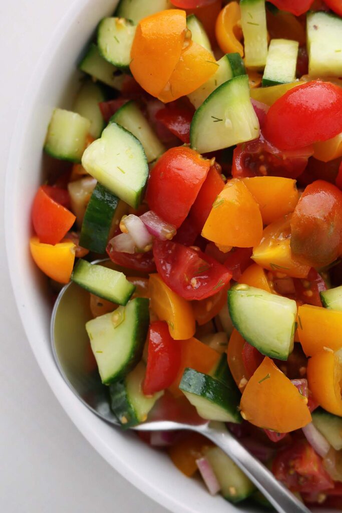close up image showing chopped cucumber, tomato and onion in a white bowl