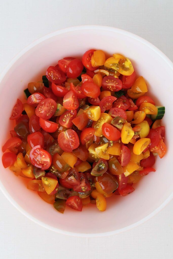 close up top down image showing chopped cucumbers in a bowl with tomatoes on top