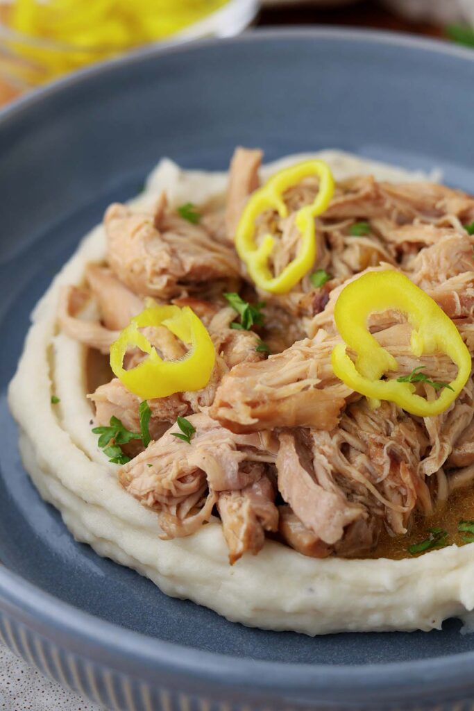 close up image showing a blue bowl with mashed potatoes, shredded chicken, and a sauce. There are three yellow pepper slices on top