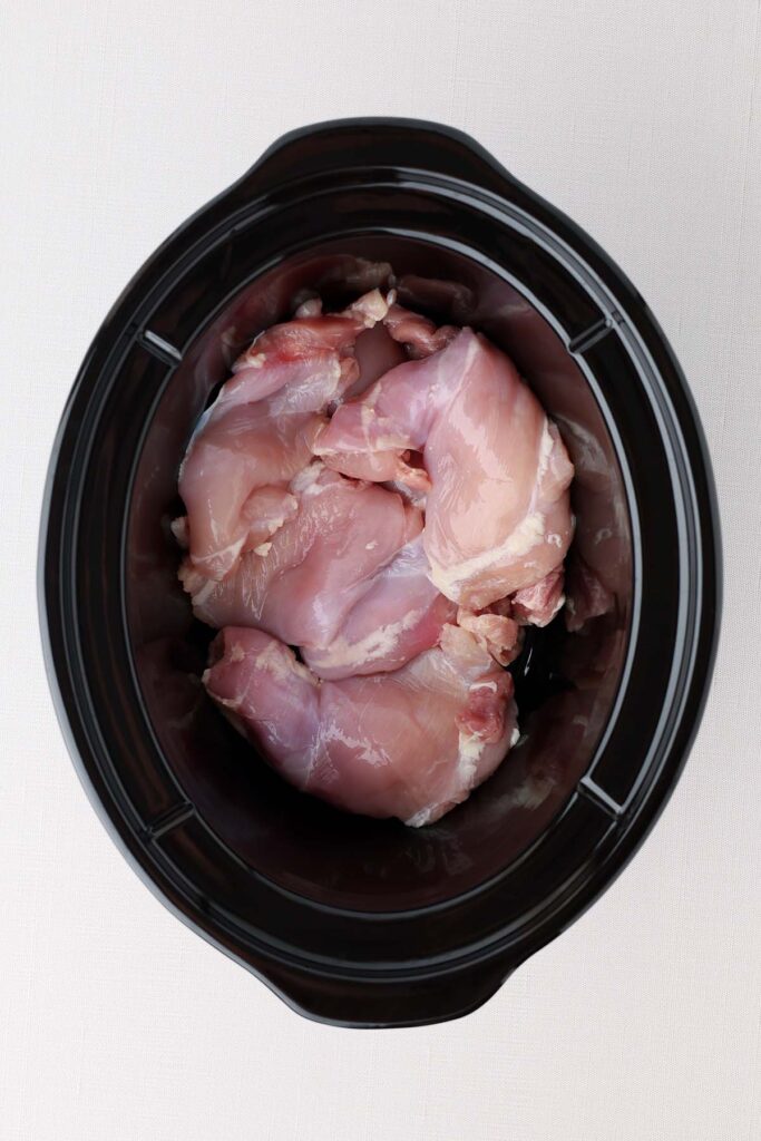 Top down image showing the inside of a black slow cooker insert. It's filled with chicken thighs
