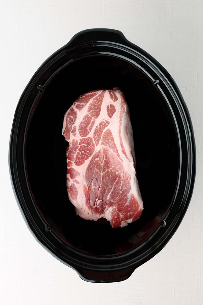 Top down image showing the inside of a slow cooker with a pork roast