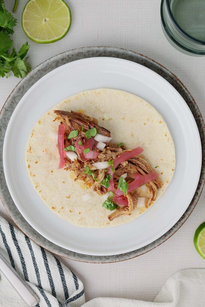 Overhead view of a pork carnitas taco topped with pickled red onions, diced onion, and chopped cilantro on a flour tortilla.