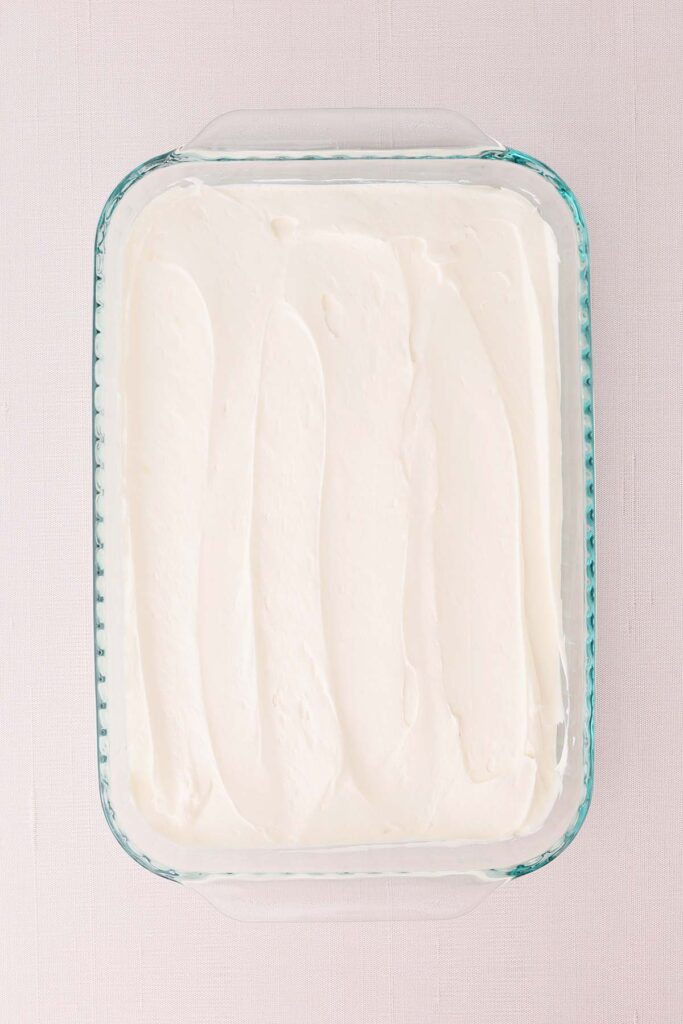 Overhead view of the creamy cheesecake layer for strawberry pretzel salad spread evenly in a glass baking dish. The smooth cream cheese and whipped topping mixture covers the pretzel crust, ready for the strawberry topping to be added.