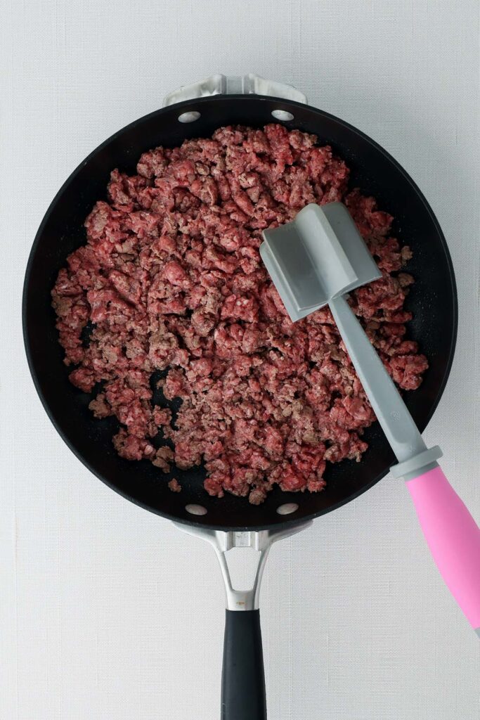 Top down image showing ground beef being cooked in a black skillet with a meat cooking spatual