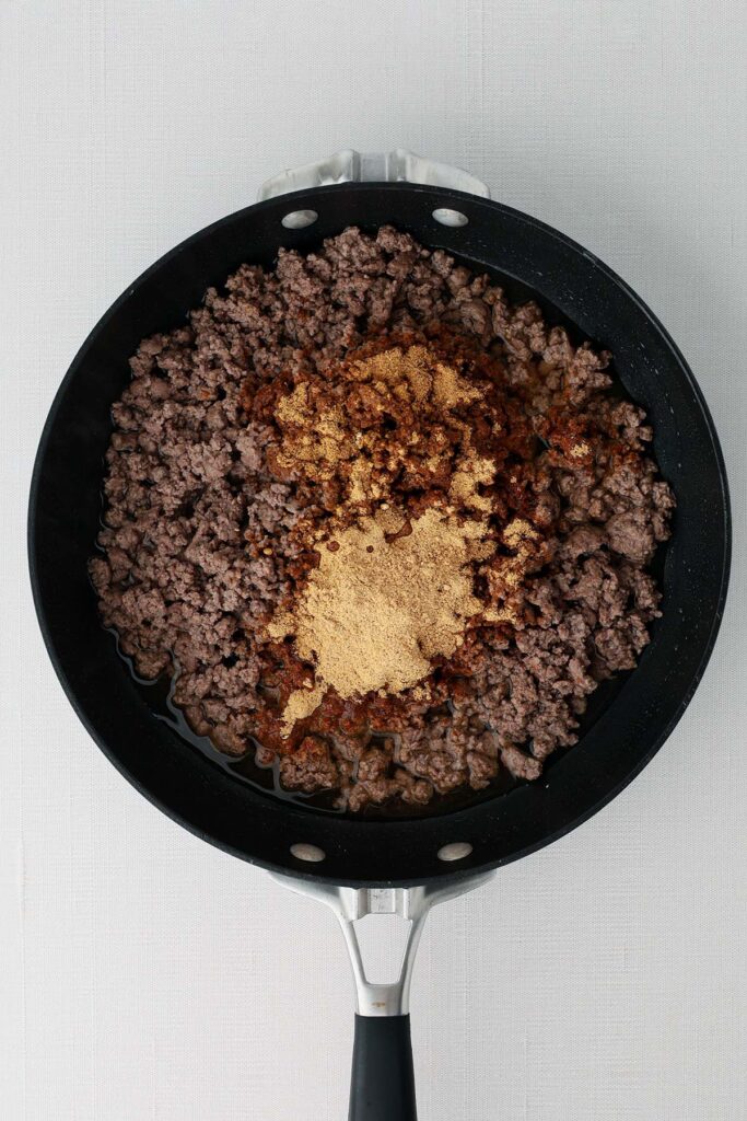 Top down showing a black skillet with cooked ground beef and seasoning unmixed