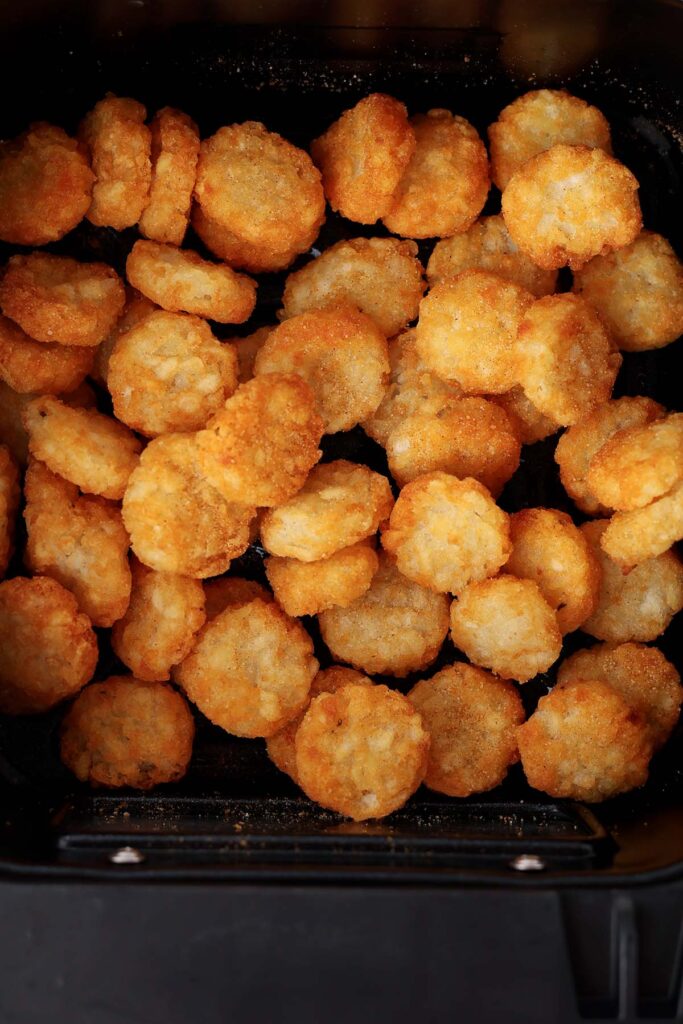Top down image showing the inside of an air fryer filled with crispy tots