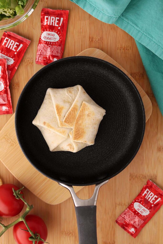 Top down image showing a small tortilla that has been folded over ingredients being grilled in a small pan