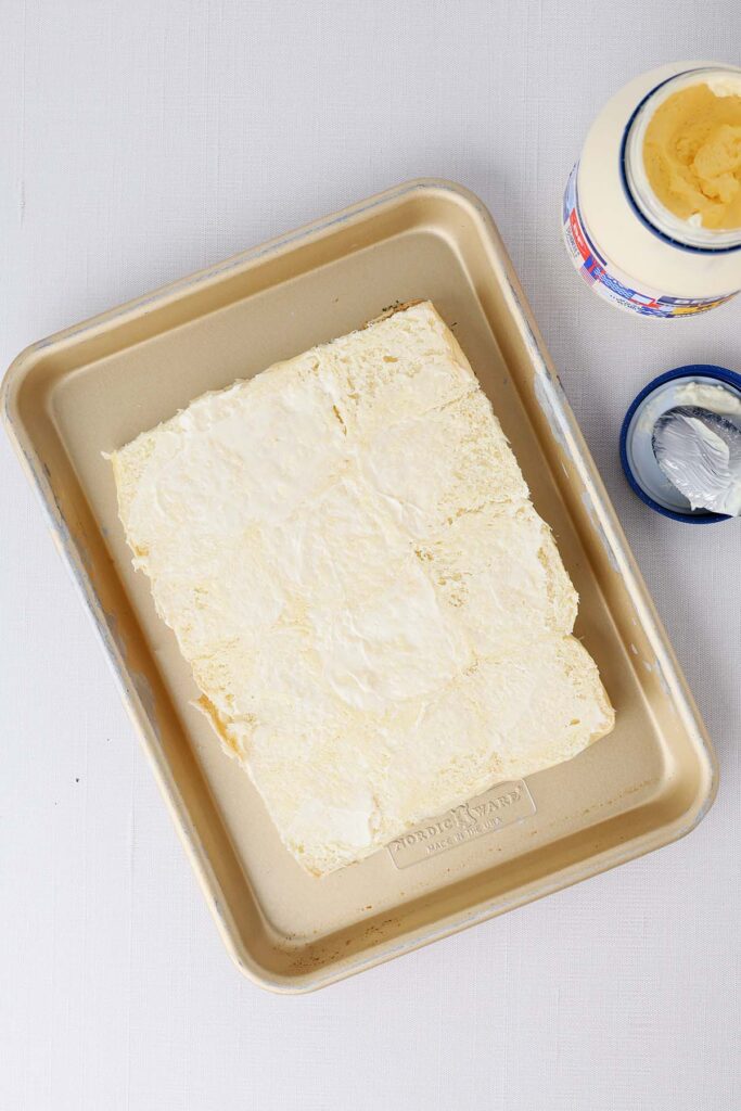 Top down image showing a sheet pan with the bottom half of hawaiian rolls spread with mayo