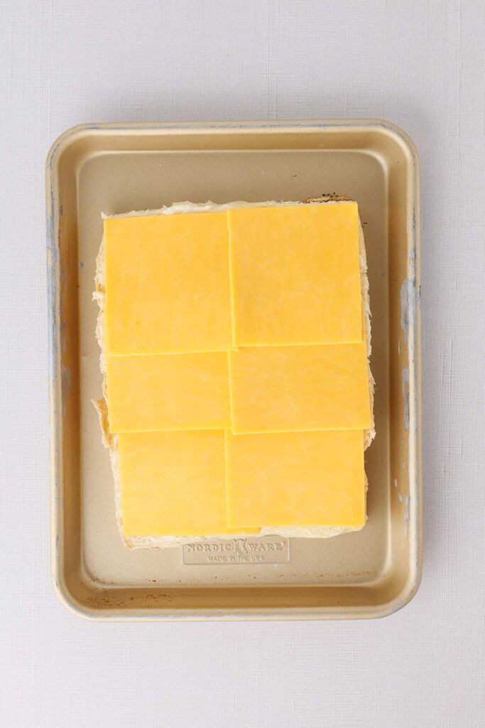 Top down image showing a small sheet pan with hawaiian rolls stacked with cheese slices