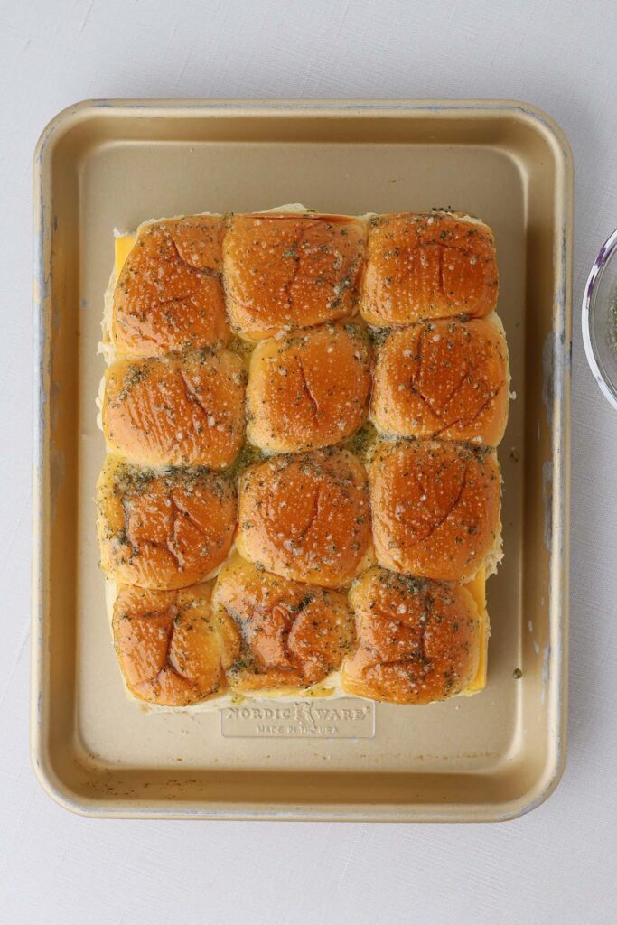 Top down image showing hawaiian rolls brushed with a garlic butter sitting on a sheet pan