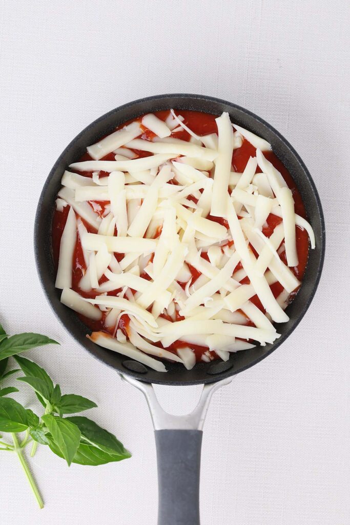 Top down image showing a small black skillet filled with sauce and cheese