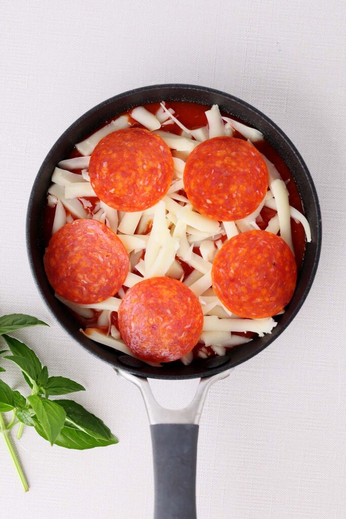 Top down image showing a small black skillet filled with sauce and cheese and pepperoni