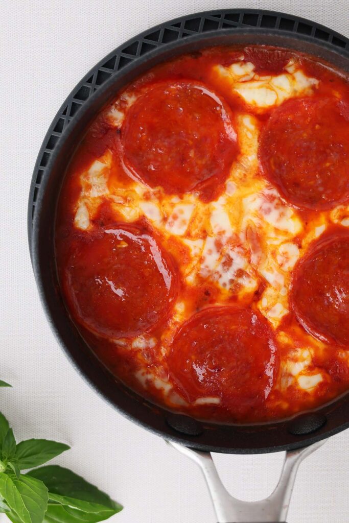 Top down image showing a small black skillet filled with sauce and melty cheese and pepperoni