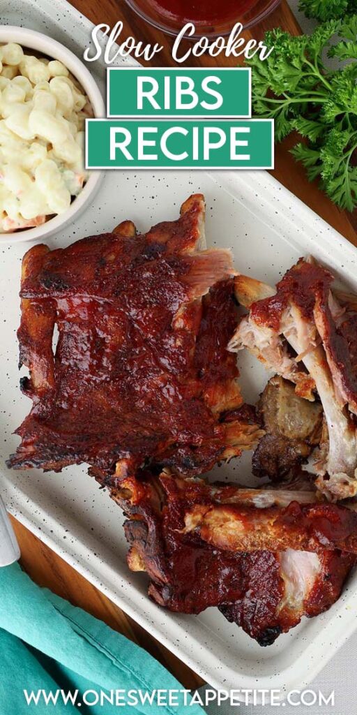 Top down image showing a white tray with ribs scattered across. There's a small bowl of macaroni salad, a fork, and some bbq sauce in a dish on the side. Text overlay reads "slow cooker ribs recipe"