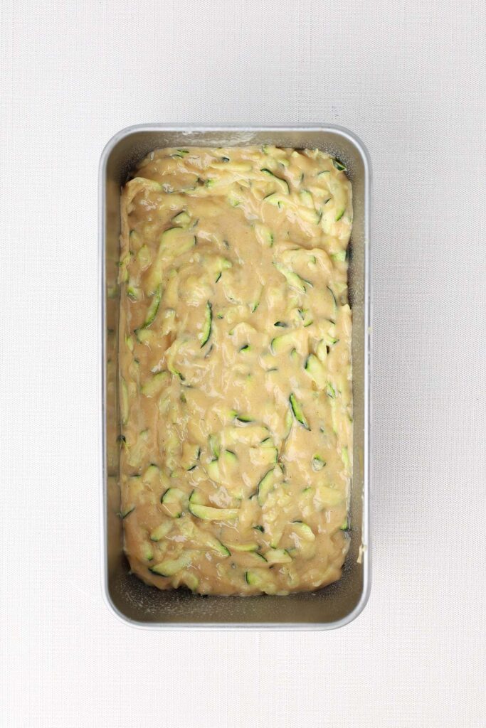 Top down image showing a bread tin filled with a zucchini batter.