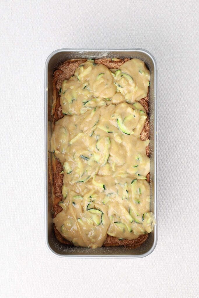 Top down image showing a bread tin filled with a zucchini batter layered on top of cinnamon sugar