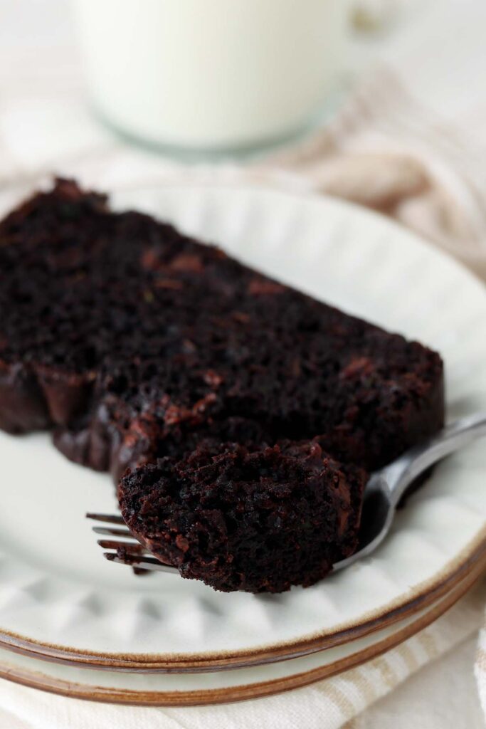 close up image showing a white plate with a chocolate loaf piece on top. There is a bite on a fork