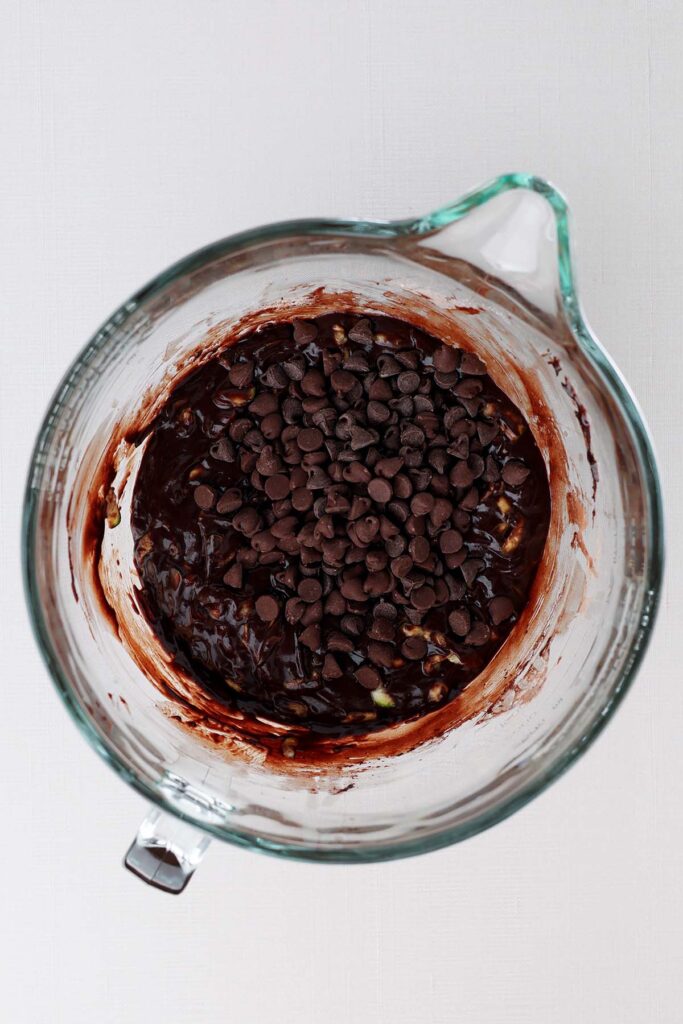 Top down image showing a glass mixing bowl with a chocolate batter and chocolate chips sprinkled on top