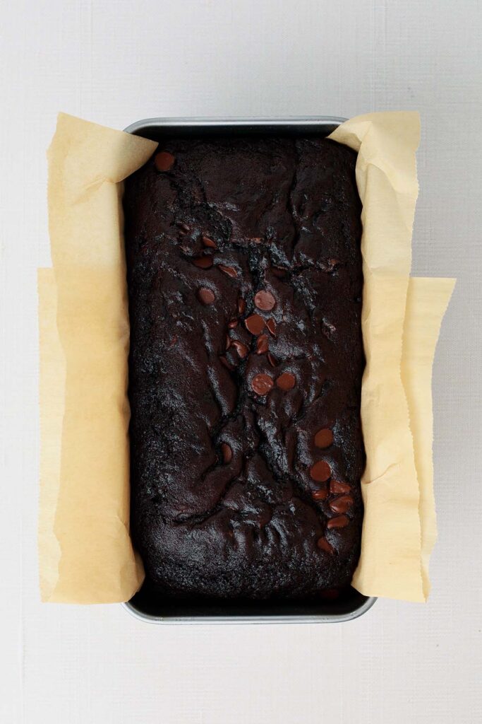 Top down image showing a chocolate loaf inside a loaf pan with brown parchment paper sticking out of the edges