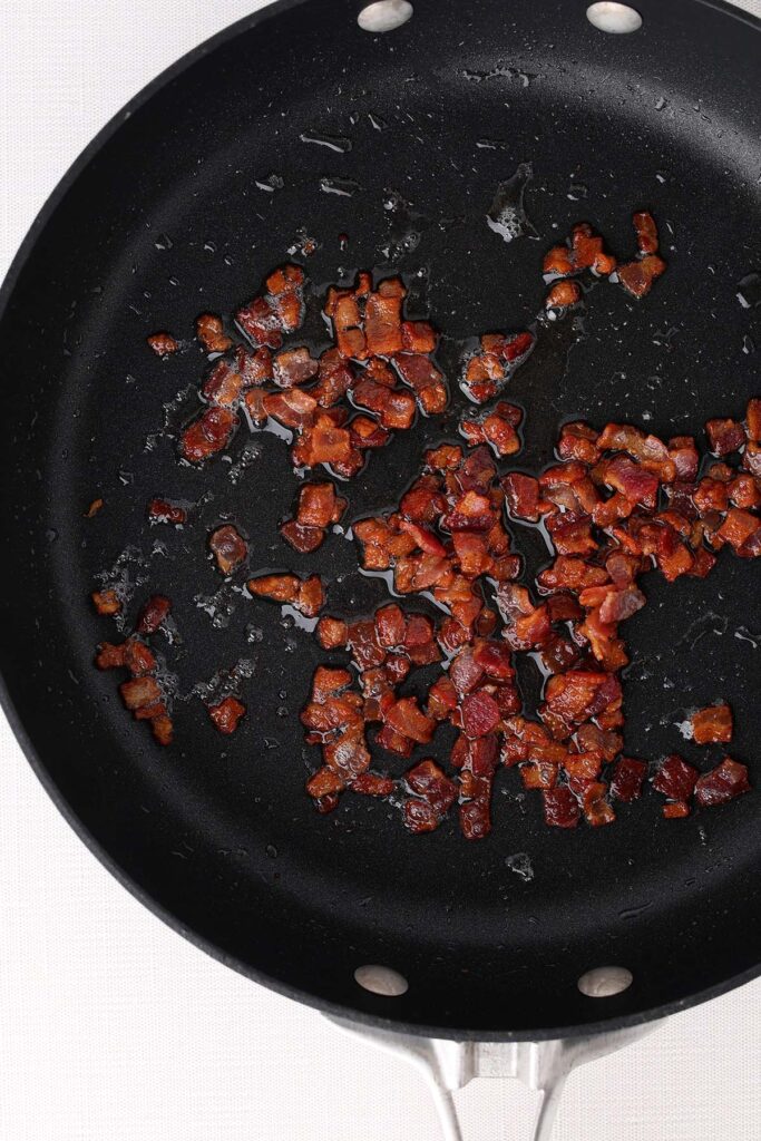 close up top down image showing a black skillet with cooked chopped bacon pieces