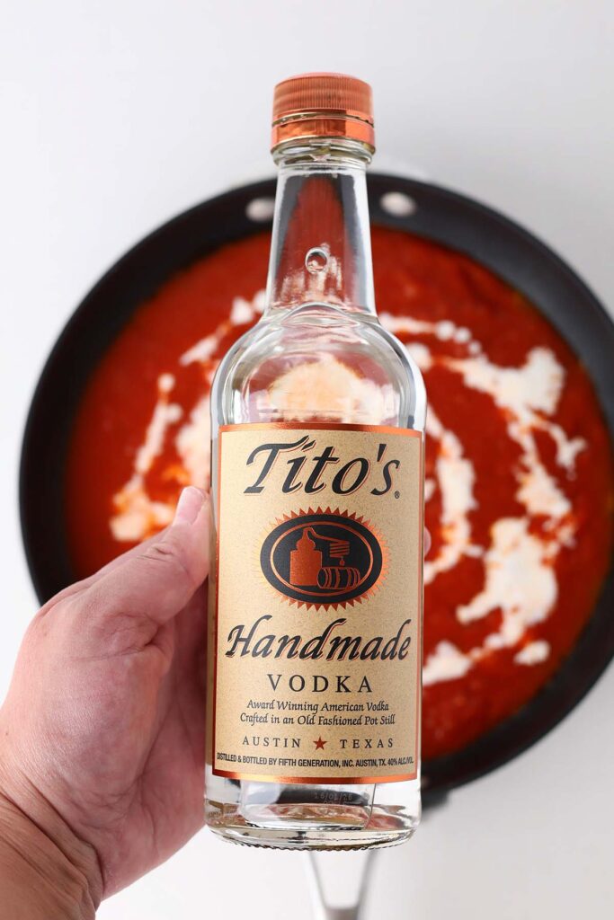 Top down image showing a bottle of Titos handmade vodka over a pan of red sauce