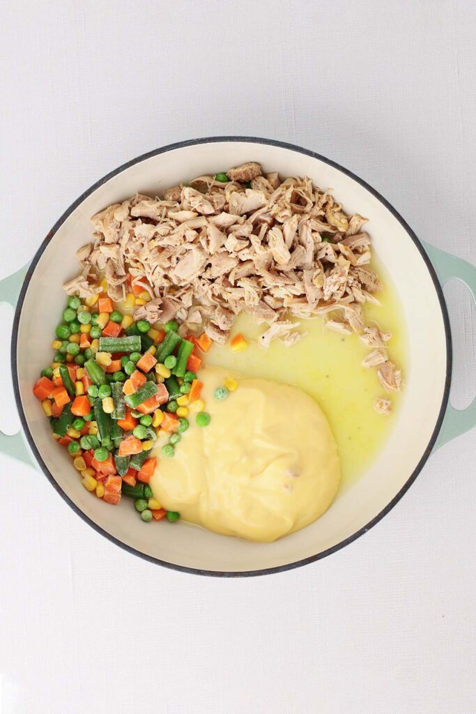 Top down image showing the inside of a skillet with cream of chicken soup, mixed veggies, chicken that's cooked and shredded and chicken broth unmixed