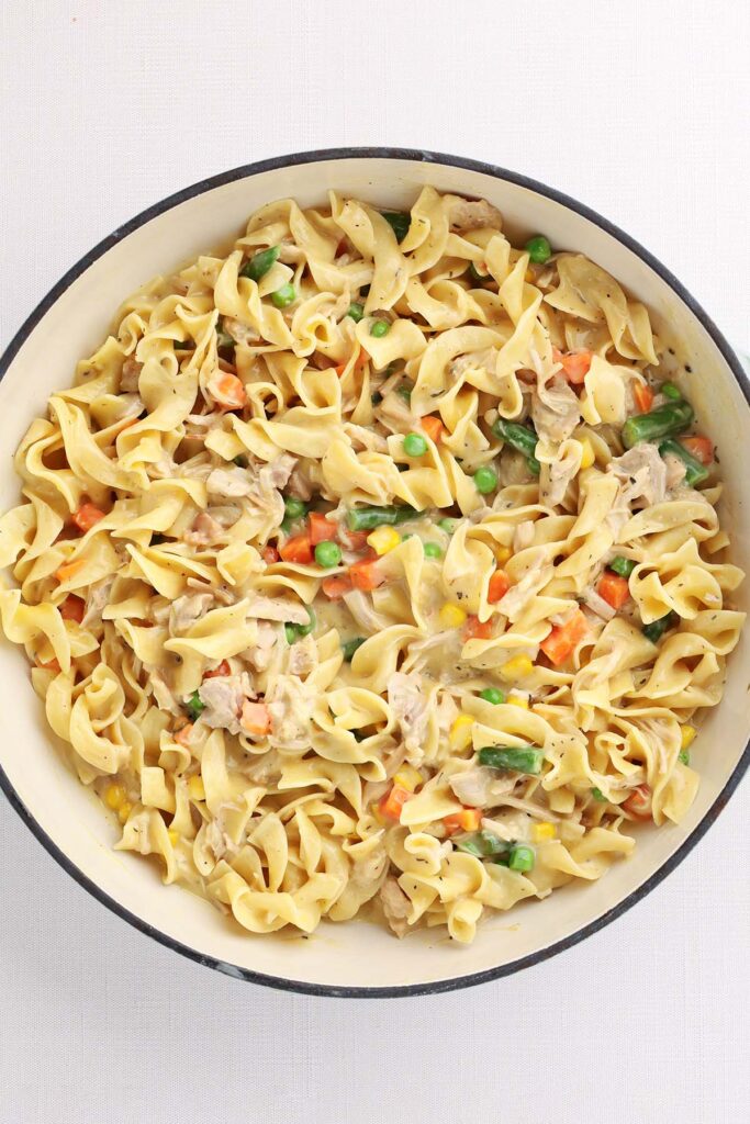 Close up shot of a pot of noodles in a creamy sauce with chicken and mixed veggies