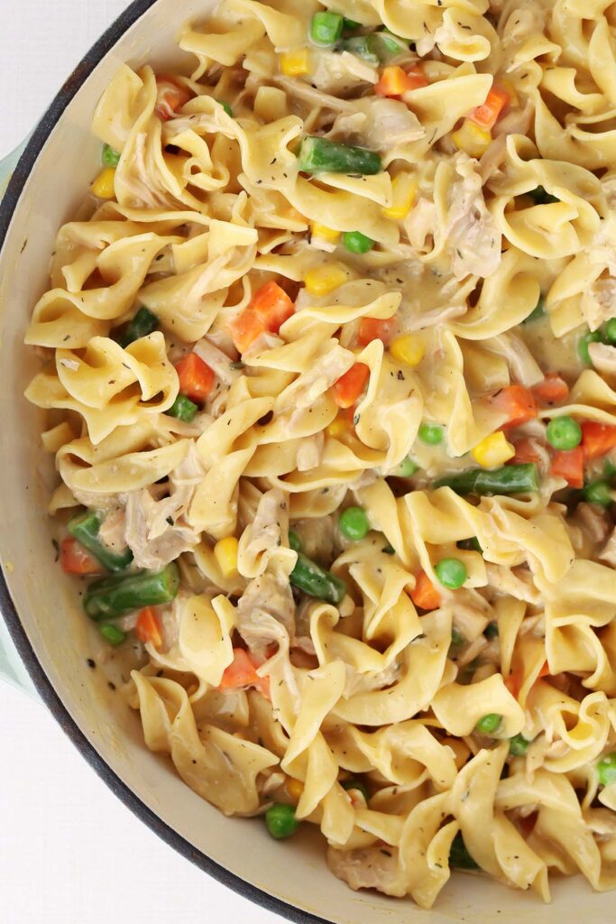 Close up shot of a pot of noodles in a creamy sauce with chicken and mixed veggies