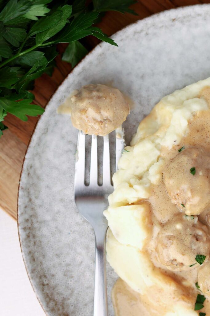 top down image showing a fork with a meatball in gravy. There are more meatballs and mashed potatoes off to the side